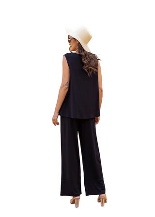 Woman in a black outfit and white hat standing in front of a textured wall.