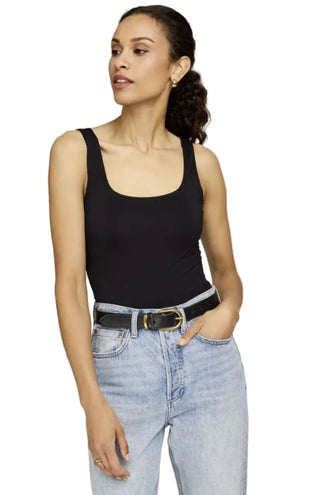 Woman wearing a black tank top and light blue jeans on a plain background