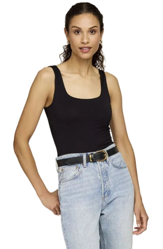 Woman wearing a black tank top and light blue jeans on a plain background