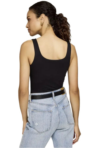 Woman wearing a black tank top and light blue jeans on a plain background