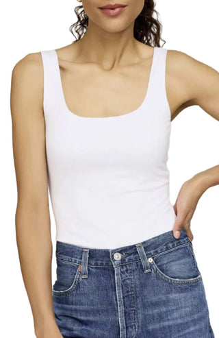 Person wearing a white tank top and blue jeans against a plain background