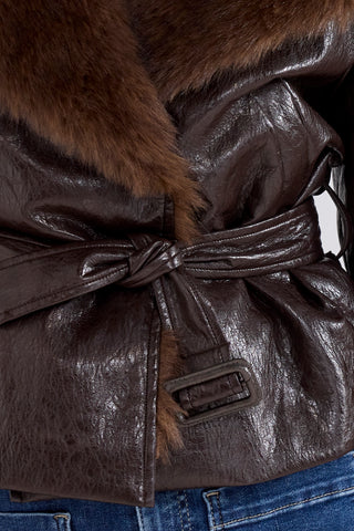 Close-up of a dark brown faux-crocodile leather jacket with a matching tie belt and a thick brown fur collar, worn over blue jeans.