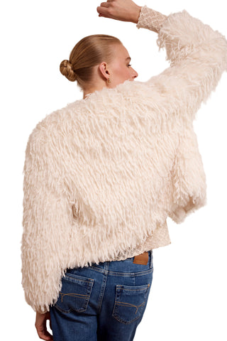 Person wearing a fluffy white jacket and blue jeans on a plain background