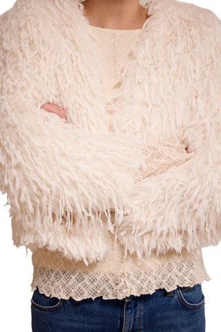 Close-up of a person wearing a cream-colored shaggy sweater over a lace top with blue jeans.