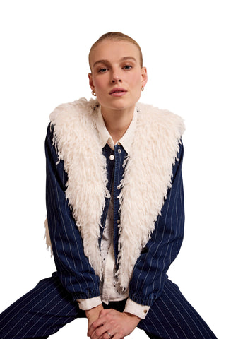 Person wearing a blue pinstripe outfit with a white fur vest against a plain background