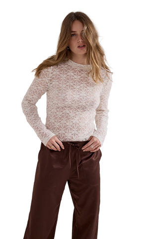 A woman modeling a cream-colored knit sweater with a textured geometric pattern, paired with dark brown wide-leg trousers, against a plain light gray studio background.