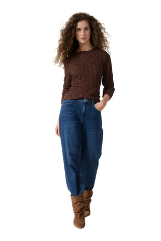 A woman modeling a brown textured knit long-sleeve top, blue wide-leg jeans, and brown suede boots against a plain white studio background.