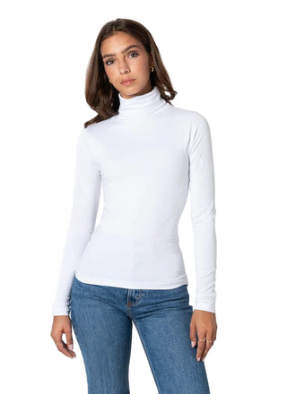 Woman wearing a white turtleneck sweater and blue jeans on a white background