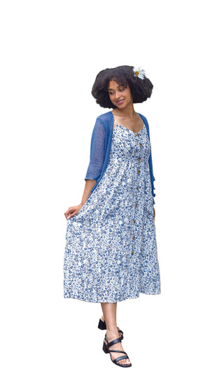 Woman in a floral dress and blue cardigan standing in a garden setting.