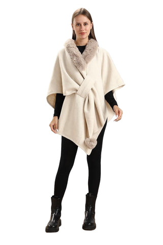 Woman wearing a cream-colored poncho with fur trim and black leggings on a wooden floor.