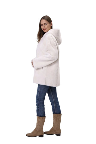 Woman wearing a white coat, blue jeans, and brown boots on a light gray background