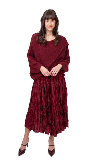 Woman wearing a burgundy outfit with a sweater and pleated skirt on a white background