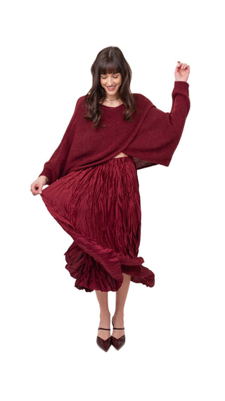 Woman wearing a burgundy outfit with a long-sleeve top and pleated skirt on a white background