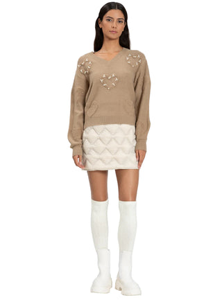 Woman wearing a beige sweater with star patterns and a white quilted skirt on a white background