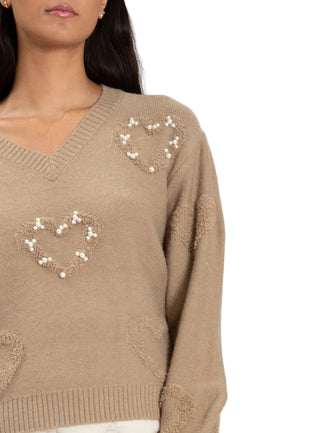 Beige sweater with heart patterns on a plain background