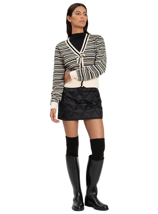 Woman wearing a striped cardigan, black top, black skirt, and black knee-high boots on a white background