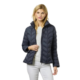 A woman modeling a dark navy blue quilted puffer jacket over a white top and white pants, standing against a neutral gray studio background.