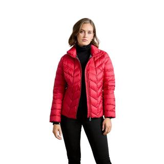 A woman modeling a bright red quilted puffer jacket over a black turtleneck and black pants, standing against a neutral light gray studio background.