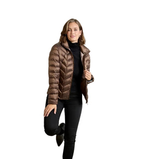 A woman modeling a metallic bronze quilted puffer jacket over a black turtleneck and black pants, posing against a neutral light gray studio background.