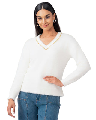 Woman wearing a white sweater and blue jeans against a white curtain background