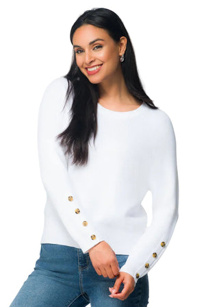 Woman wearing a white blouse with gold buttons and blue jeans, standing next to a floral arrangement.