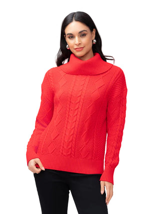 A woman modeling a bright red cable-knit mock neck sweater with black pants, photographed against a neutral light gray studio background.