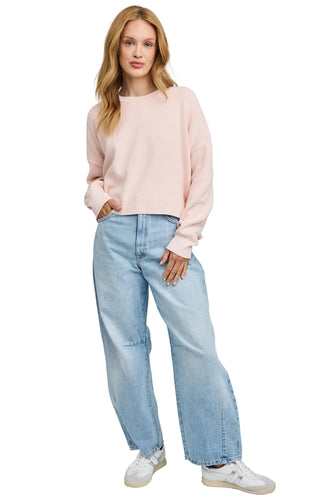 Woman wearing a light pink sweater and blue jeans on a gray background