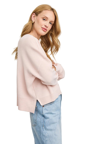 Woman wearing a light pink sweater and blue jeans on a plain background