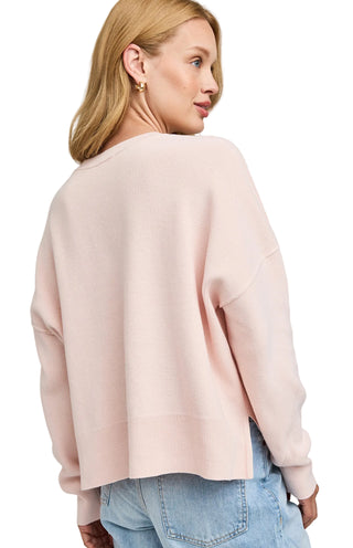 Woman wearing a light pink sweater and blue jeans on a gray background