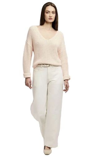Woman wearing a light pink sweater and white pants on a plain background