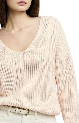 Close-up of a person wearing a light pink knitted sweater on a plain background