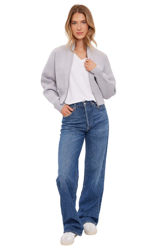 Woman wearing a gray cardigan, white shirt, and blue jeans on a white background