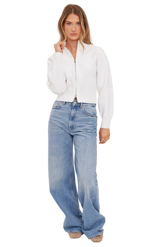 Woman wearing a white blouse and light blue jeans on a plain background