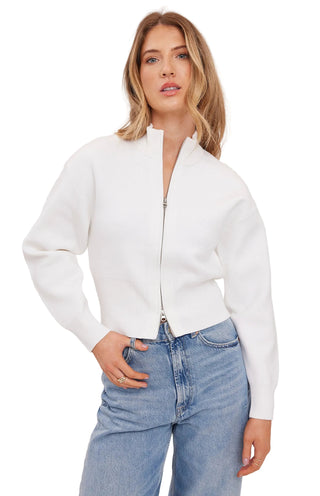 Woman wearing a white zip-up sweatshirt and blue jeans on a plain background