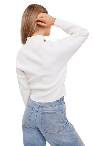Person wearing a white sweater and light blue jeans on a plain background