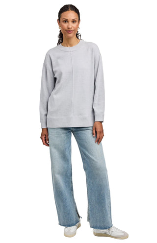 Woman wearing a light gray sweater and blue jeans on a plain background