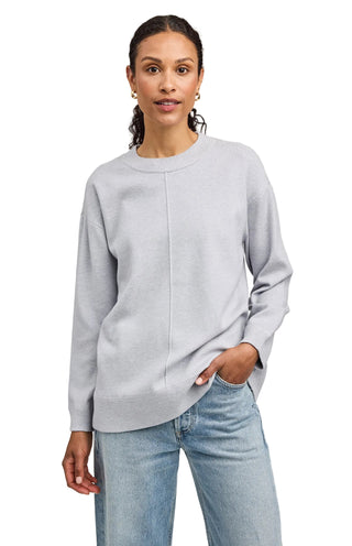 Woman wearing a light gray sweater and blue jeans against a plain background