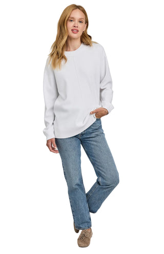 Woman wearing a white sweater and blue jeans on a plain background
