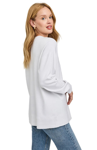 Woman wearing a light gray sweater and blue jeans on a plain background