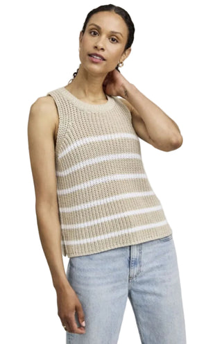 Woman wearing a beige and white striped sleeveless top with light blue jeans on a plain background
