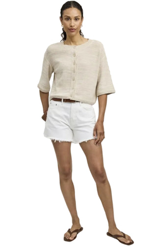 Woman wearing a beige cardigan and white shorts on a plain background