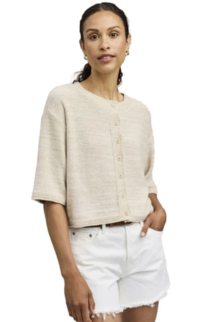 Woman wearing a beige cardigan and white shorts against a plain background