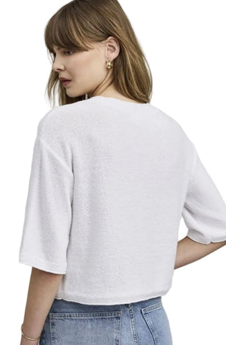 Woman wearing a white sweater and blue jeans against a plain background