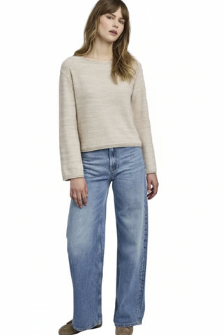 Woman wearing a beige sweater and blue jeans on a plain background