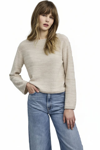 Woman wearing a beige sweater and blue jeans on a plain background