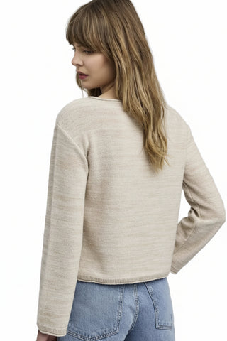 Woman wearing a beige sweater and blue jeans on a plain background