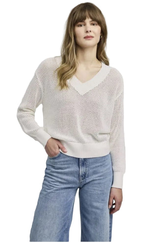 Woman wearing a light pink sweater and blue jeans against a plain background