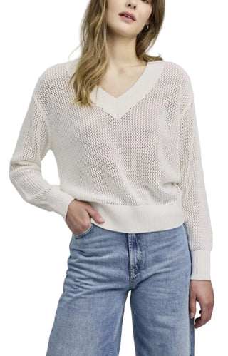 Woman wearing a white knit sweater and blue jeans on a gray background