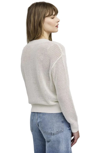 Woman wearing a light-colored knitted sweater and blue jeans on a plain background