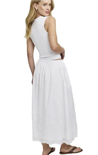 Woman wearing a white sleeveless top and skirt on a plain background